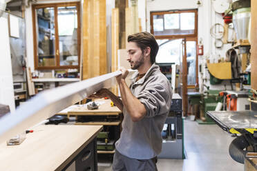 Junger männlicher Tischler trägt Holz bei der Arbeit in der Werkstatt - MEUF03554