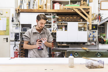 Young male craftsperson holding drill while working in workshop - MEUF03555