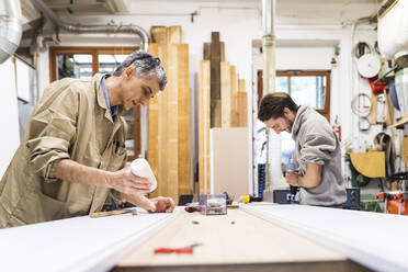 Älterer männlicher Eigentümer und Kollege bei der Arbeit am Tisch in der Werkstatt - MEUF03558