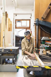 Mature male carpenter using machine while working at workshop - MEUF03566