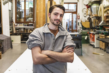 Young male craftsperson with arms crossed at workshop - MEUF03569