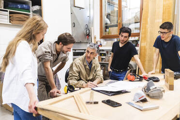 Ein Team von Schreinern diskutiert am Tisch in der Werkstatt - MEUF03585