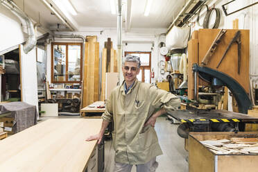 Lächelnder männlicher Tischler mit Hand auf der Hüfte in der Werkstatt - MEUF03617