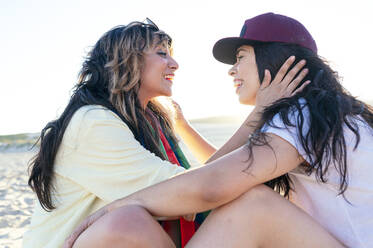 Lesbisches Paar schaut sich am Strand sitzend an - JCMF02122