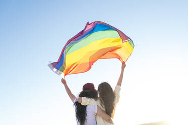 Unbeschwerte junge Lesben, die eine Regenbogenfahne in der Hand halten - JCMF02124