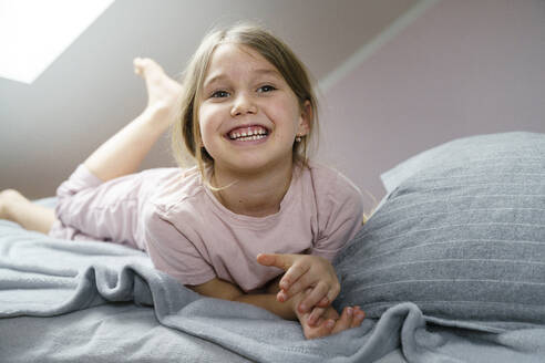 Smiling girl lying on bed at home - KMKF01722