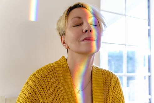 Woman in yellow sweater with spectrum on face at home - KMKF01726