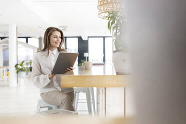 Weibliche Fachkraft mit digitalem Tablet auf einem Tisch im Büro sitzend - PESF02960