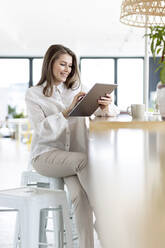 Berufstätige Frau, die im Büro sitzend ein digitales Tablet benutzt - PESF02962