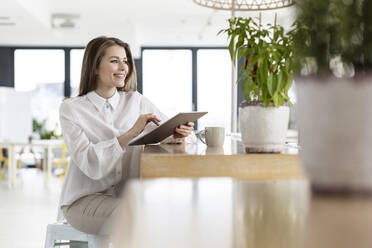 Lächelnde weibliche Fachkraft mit digitalem Tablet im Büro sitzend - PESF02963