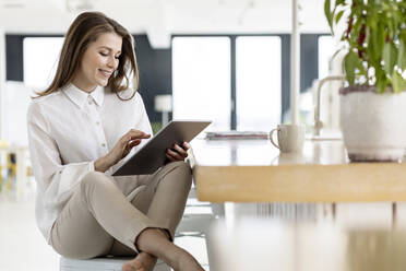 Geschäftsfrau, die ein digitales Tablet benutzt, während sie am Tisch im Büro sitzt - PESF02964