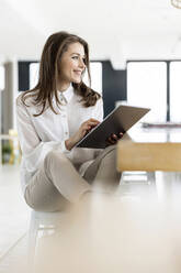 Weibliche Fachkraft mit digitalem Tablet, die im Büro sitzt und nachdenkt - PESF02965