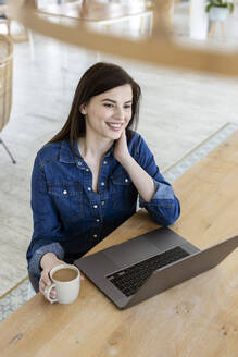 Nachdenkliche Geschäftsfrau mit Laptop, die am Tisch im Büro sitzt - PESF02966