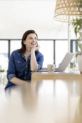 Thoughtful businesswoman with hand on chin sitting by laptop at workplace - PESF02972