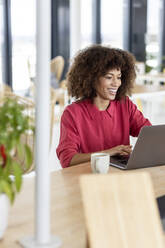 Smiling businesswoman using laptop while working at office - PESF02974