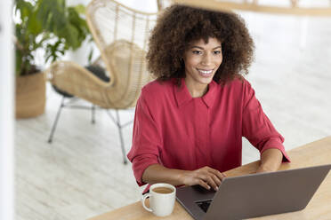 Smiling businesswoman with laptop sitting at workplace - PESF02978
