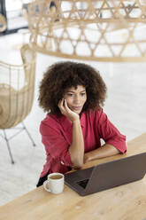 Nachdenkliche Geschäftsfrau mit Hand am Kinn, die im Büro am Laptop sitzt - PESF02979