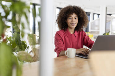 Afro businesswoman with laptop smiling in office - PESF02980