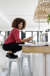 Smiling businesswoman with digital tablet crouching on table - PESF02982