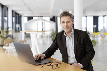 Businessman with laptop sitting by table at office - PESF03013