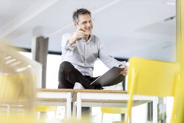 Lächelnder Geschäftsmann, der mit einem digitalen Tablet am Arbeitsplatz sitzt und darauf zeigt - PESF03025