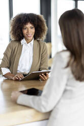 Weibliche Fachkraft, die ein digitales Tablet hält und mit einem Kollegen im Büro diskutiert - PESF03035
