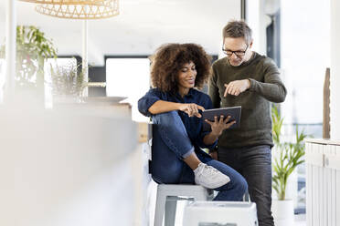 Lächelnde junge Geschäftsfrau, die mit einem männlichen Fachmann über ein digitales Tablet im Büro diskutiert - PESF03059