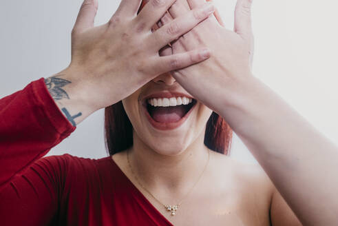 Lächelnde Frau, die ihre Augen mit den Händen vor einem weißen Hintergrund bedeckt - DSIF00517