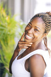 Woman with braided hair smiling while touching face - OCMF02185