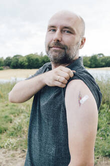 Vaccinated man showing bandage by tattoo on arm - KMKF01740