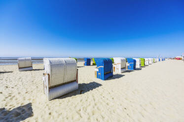 Klarer blauer Himmel über Reihen von Strandkörben mit Kapuze, die im Sommer am Sandstrand stehen - THAF02985