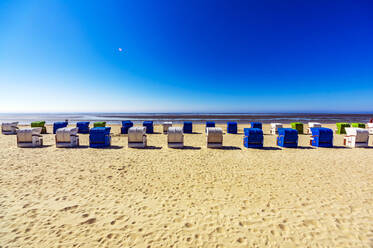 Klarer blauer Himmel über Reihen von Strandkörben mit Kapuze, die im Sommer am Sandstrand stehen - THAF02986