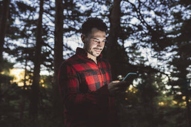 Mann benutzt Smartphone im Wald stehend - JCCMF03173