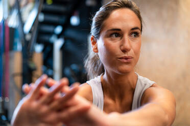 Fit female athlete in sportswear doing exercise in gym looking away - ADSF27094