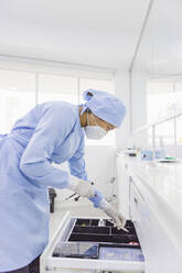 Seitenansicht einer Kieferorthopädin, die sich über eine Schublade mit medizinischen Instrumenten bei der Arbeit im Krankenhaus beugt - ADSF27103