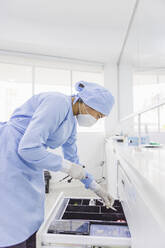 Side view of female orthodontist leaning forward above drawer with medical instruments at work in hospital - ADSF27103