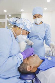 Stomatologin in Uniform und Atemmaske bei der Zahnbehandlung eines männlichen Patienten im Krankenhaus - ADSF27111