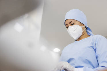 Junge Sanitäterin mit steriler Maske und Kappe blickt bei der Arbeit im Krankenhaus nach unten - ADSF27112