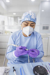 Professional female dentist in sterile uniform and gloves working with drilling machine in dental clinic - ADSF27114