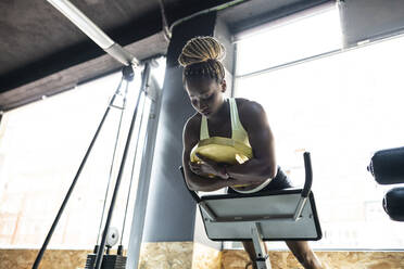 From below of fit African American female athlete performing abdominal exercise on hyperextension bench in gymnasium - ADSF27139