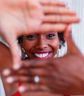 Afroamerikanische Frau demonstriert Fotogeste mit den Händen, während sie in die Kamera schaut - ADSF27146