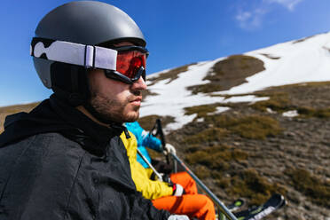Bärtiger männlicher Sportler mit Sportbrille und Helm bewundert den Winterberg gegen anonyme Partner an einem sonnigen Tag in Spanien - ADSF27153