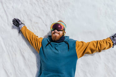 Draufsicht auf einen bärtigen Sportler mit Bart und Sportbrille, der im Schnee der Sierra Nevada in Spanien liegt - ADSF27157