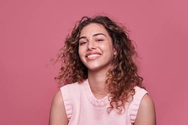 Positive junge Frau in Crop-Top und Jeans, die lächelnd in die Kamera schaut, vor einem rosa Hintergrund - ADSF27182