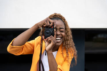 Happy African American female laughing happily with mouth opened while taking picture on photo camera - ADSF27218