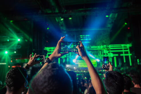 Back view anonymous people raising arms with smartphones and recording musical live performance on concert hall stage - ADSF27219