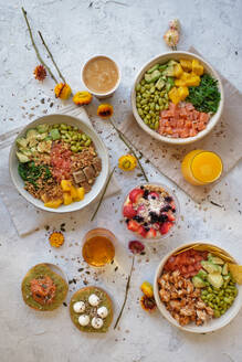Top view appetizing assorted poke bowls with avocado toasts and glasses of juices served on table with berry dessert near scattered fresh flowers - ADSF27240