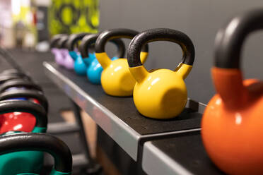 Set von bunten Kettlebells mit verschiedenen Gewichten in Reihe in einem modernen Fitness-Center platziert - ADSF27269