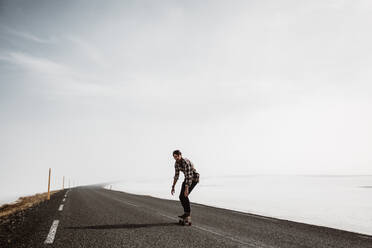 Man riding skateboard along countryside road - ADSF27289