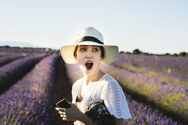 Überrascht junge Frau mit Smartphone auf Lavendelfeld - JCCMF03187